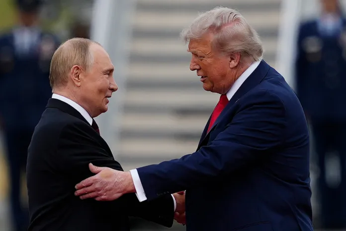 Putin and Trump face each other while shaking hands near the base of an aircraft stairway.