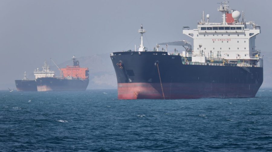 Two large tankers sit on blue water, one dominating the foreground and another visible through haze behind it.